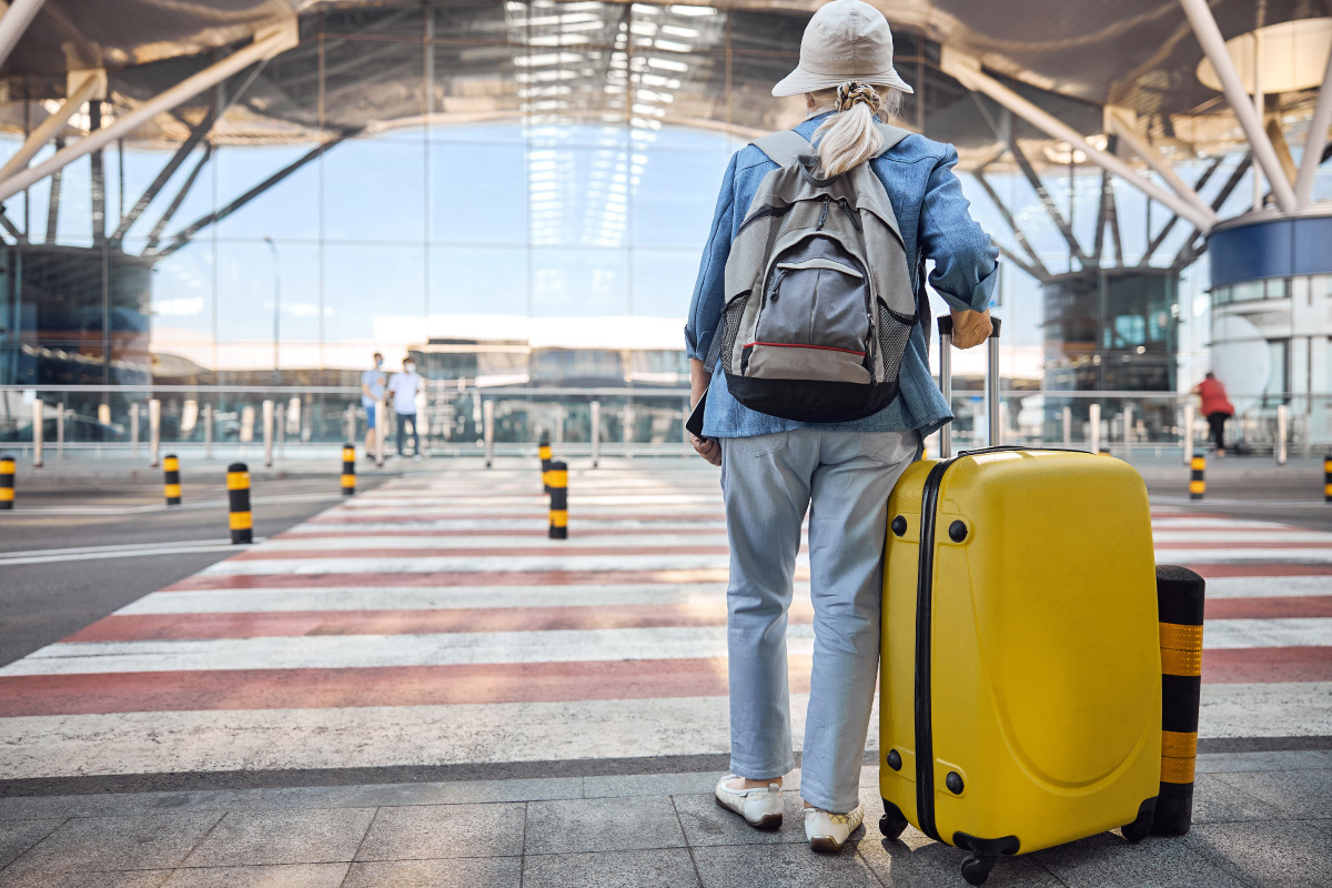 altere-frau-mit-koffer-vor-flughafen